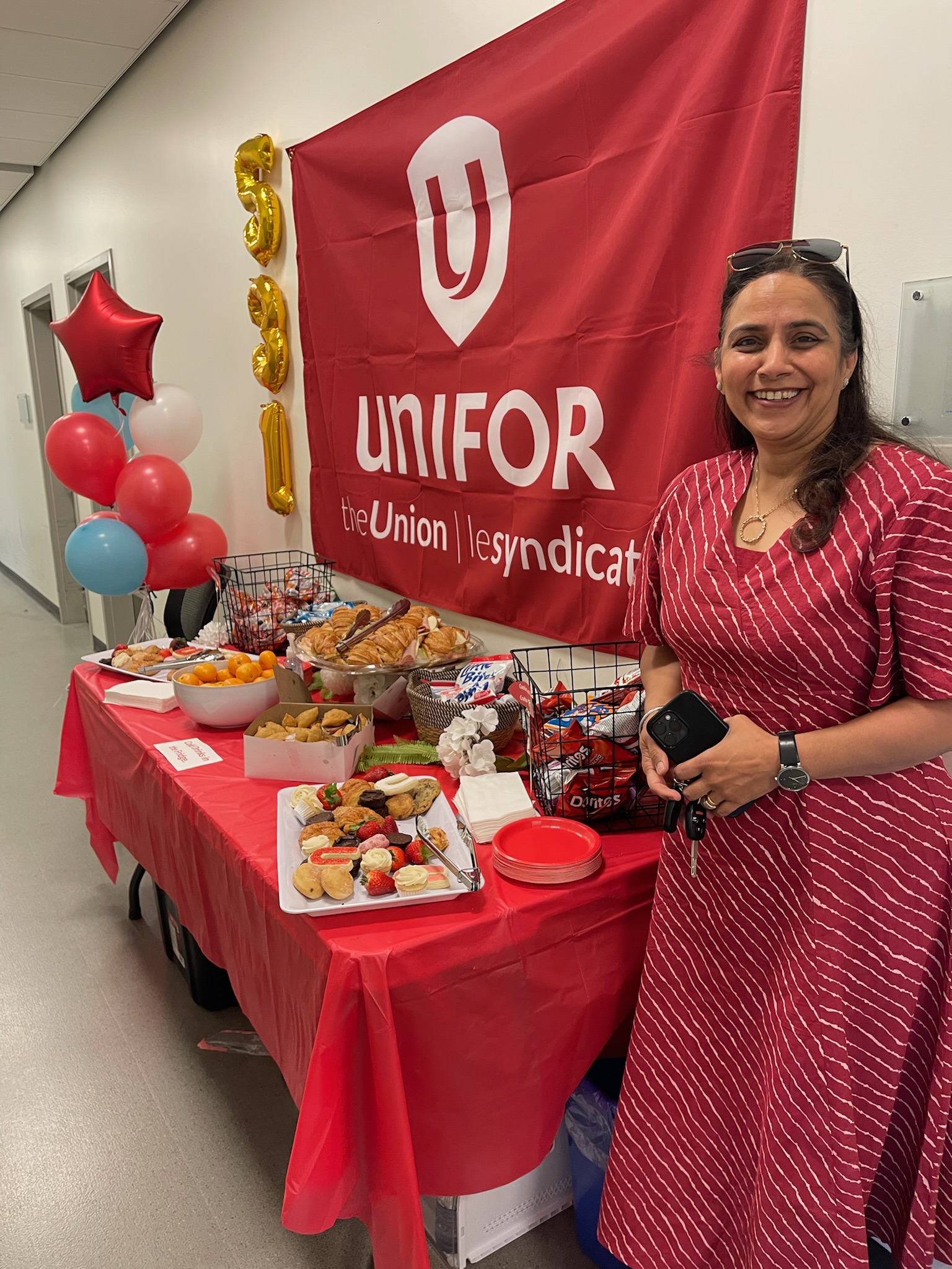 Unifor Member Jagreet standing infront of a table and unifor red flag