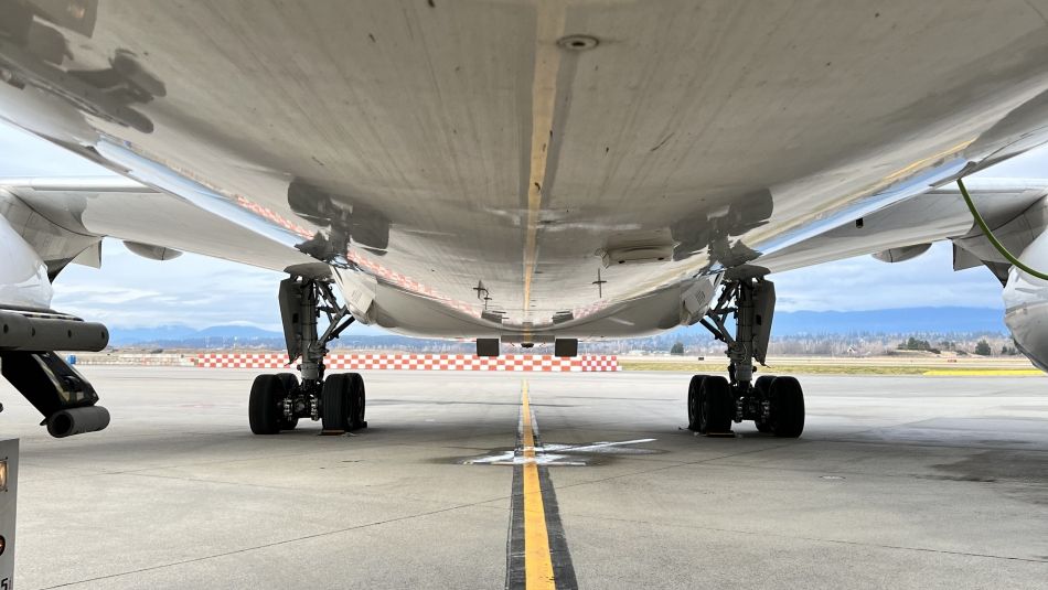 The photo shows the belly of an aircraft parked on a yellow line at the airport. 