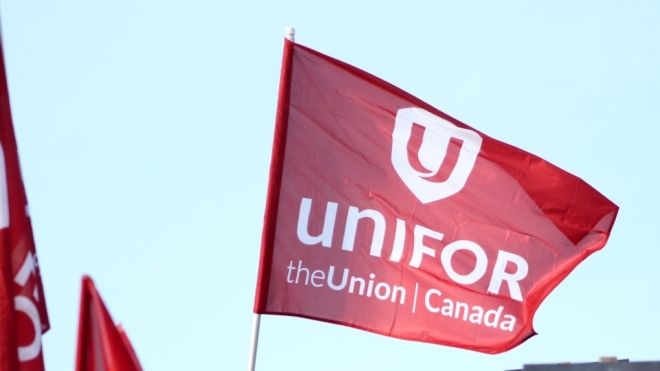 The photo shows a red flag with the work Unifor on it flying in a blue sky